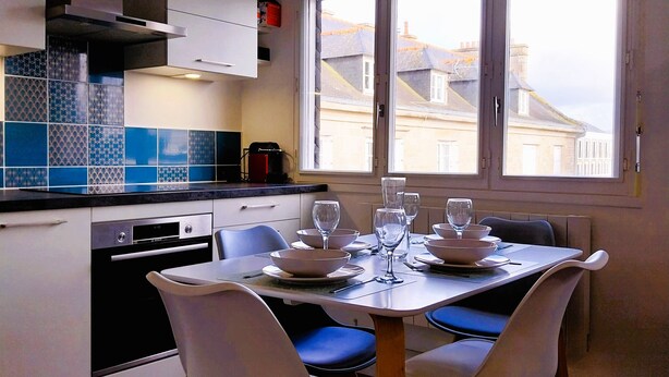 A modern kitchen with white cabinets, a black oven, and a dining table set for four with white chairs. - Charming seaside apartment (Dinard)