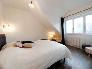 A bedroom with a bed, bedside table, lamp, window, and a view of the outdoors. - Charming seaside apartment (Dinard)