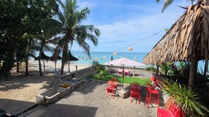 A beachside patio with red chairs, a thatched-roof structure, and a view of the ocean. - FreeDive Inn (Puerto Galera)