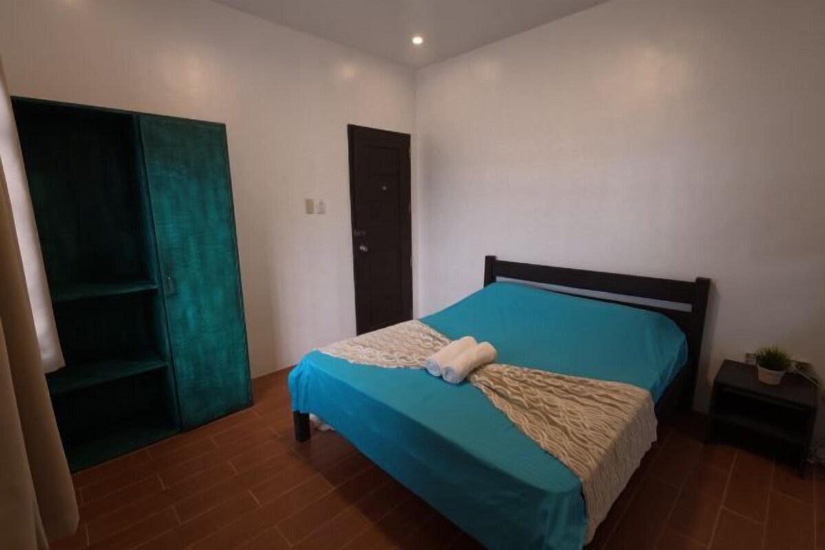 Ein Schlafzimmer mit einem Bett, einem Kleiderschrank, einer Tür und einem Nachttisch mit einer Pflanze.