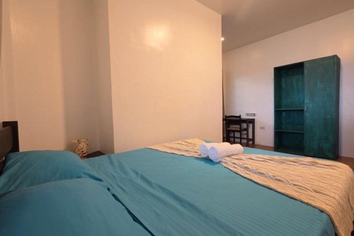 A bedroom with a bed, a nightstand, a green wardrobe, and a desk with a chair.