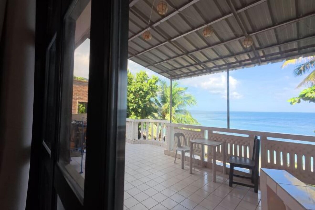 A covered outdoor area with a view of the ocean, a tiled floor, and a bench.