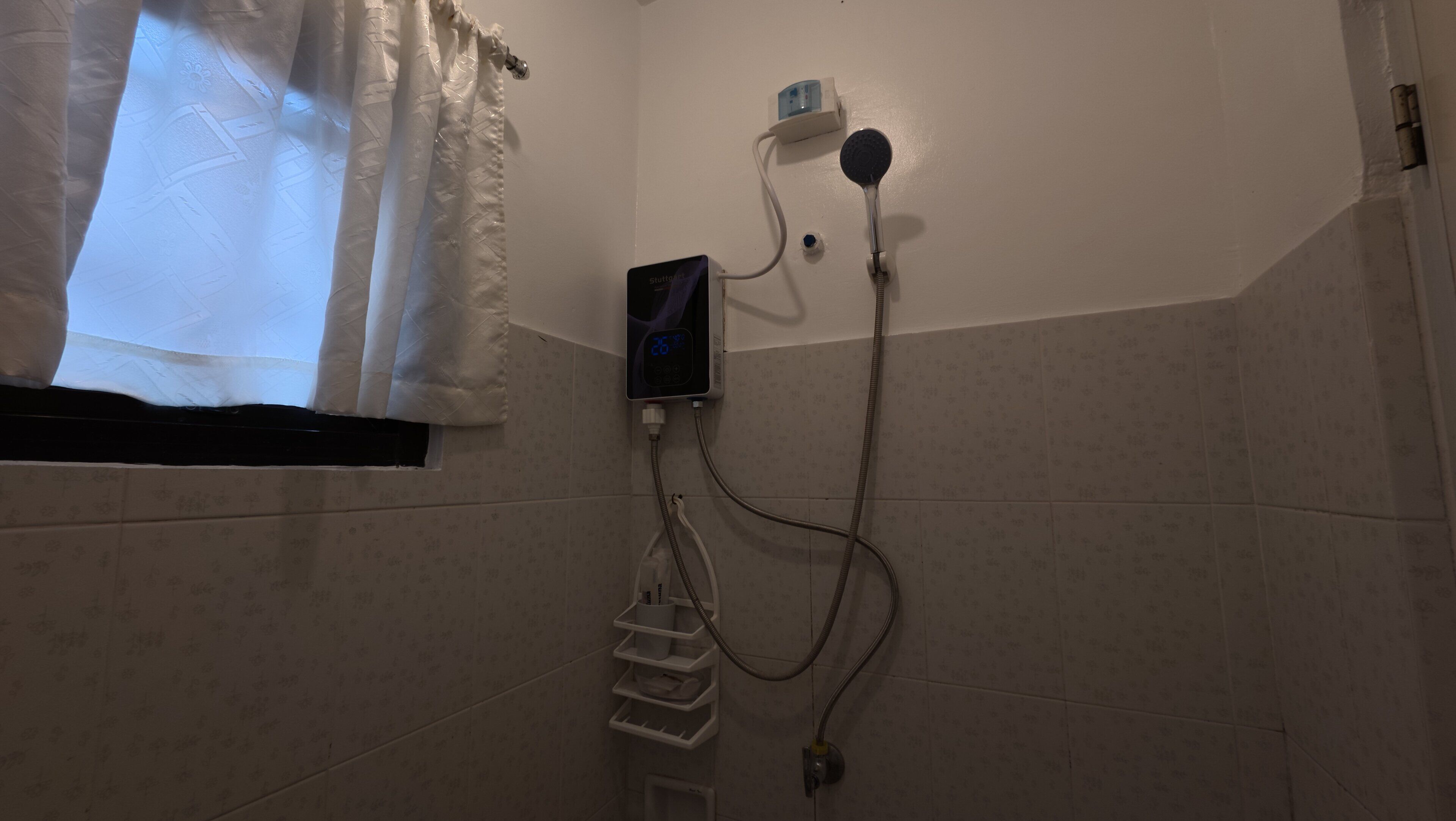 Casa de banho com chuveiro, termostato digital e janela com cortinas.