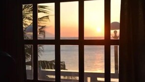 A view through a window with a wooden frame, displaying a sunset over a body of water and a distant landmass. - FreeDive Inn (Puerto Galera)