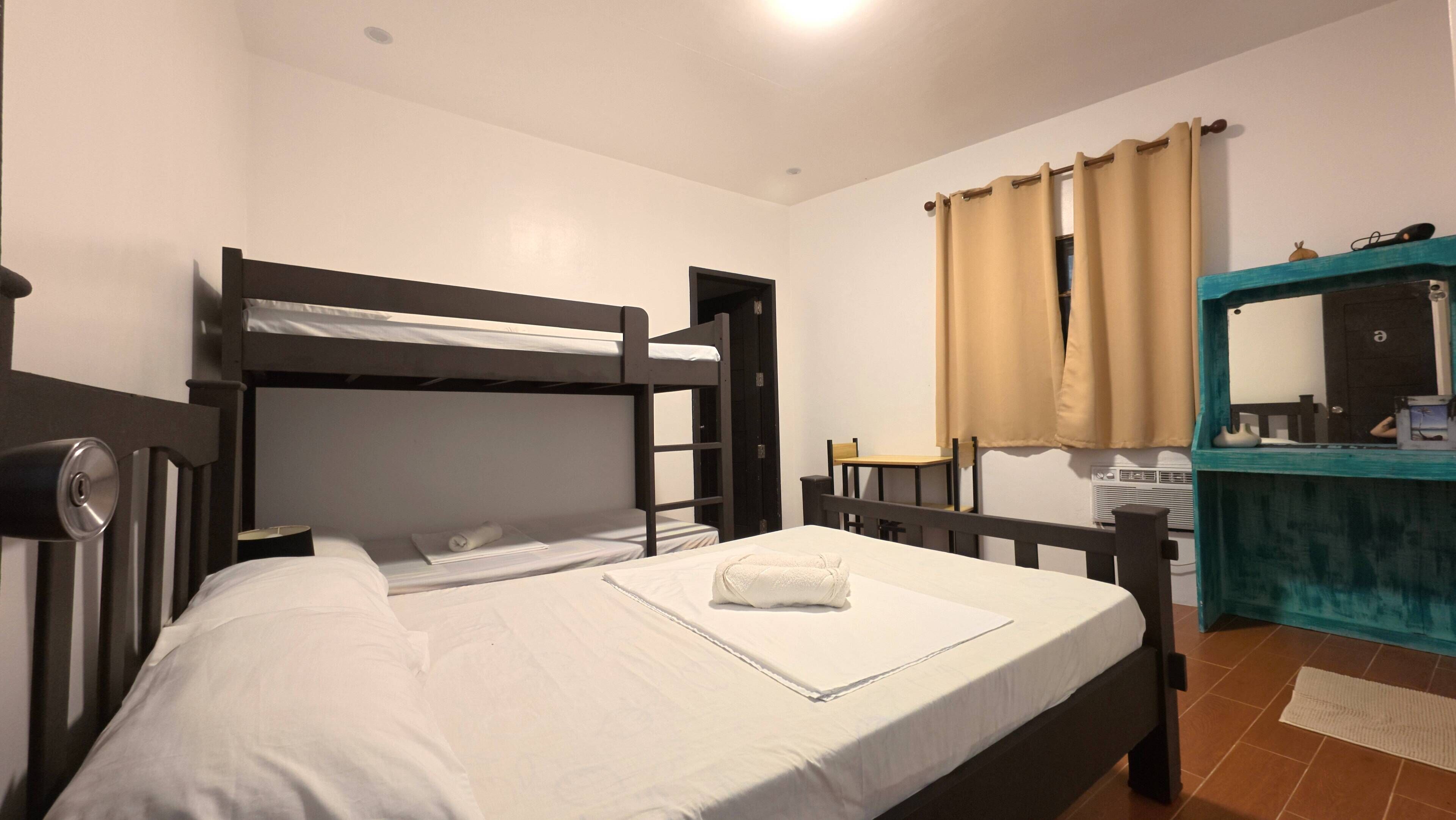 A bunk bed room with a single bed, a chair, a small table, a mirror, and a window with curtains.