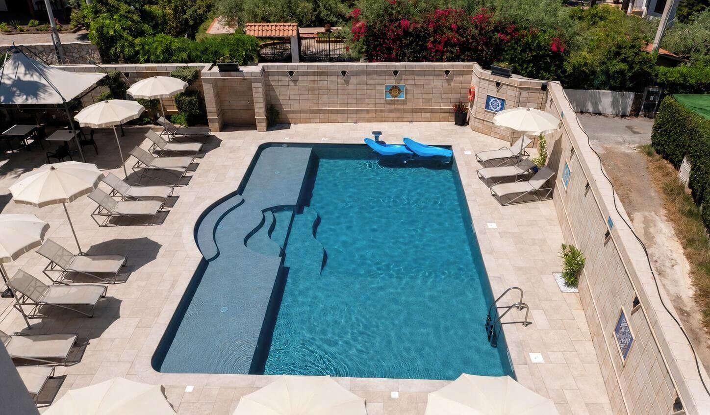 Une piscine rectangulaire avec un toboggan bleu, entourée de chaises longues et de parasols.