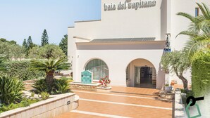 A building with a sign reading "baia del capitano" and a tiled entrance area with plants and a fountain.