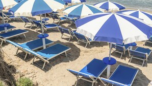 Ein Strand mit Reihen aus blau-weiß gestreiften Sonnenschirmen und angrenzenden Liegestühlen.