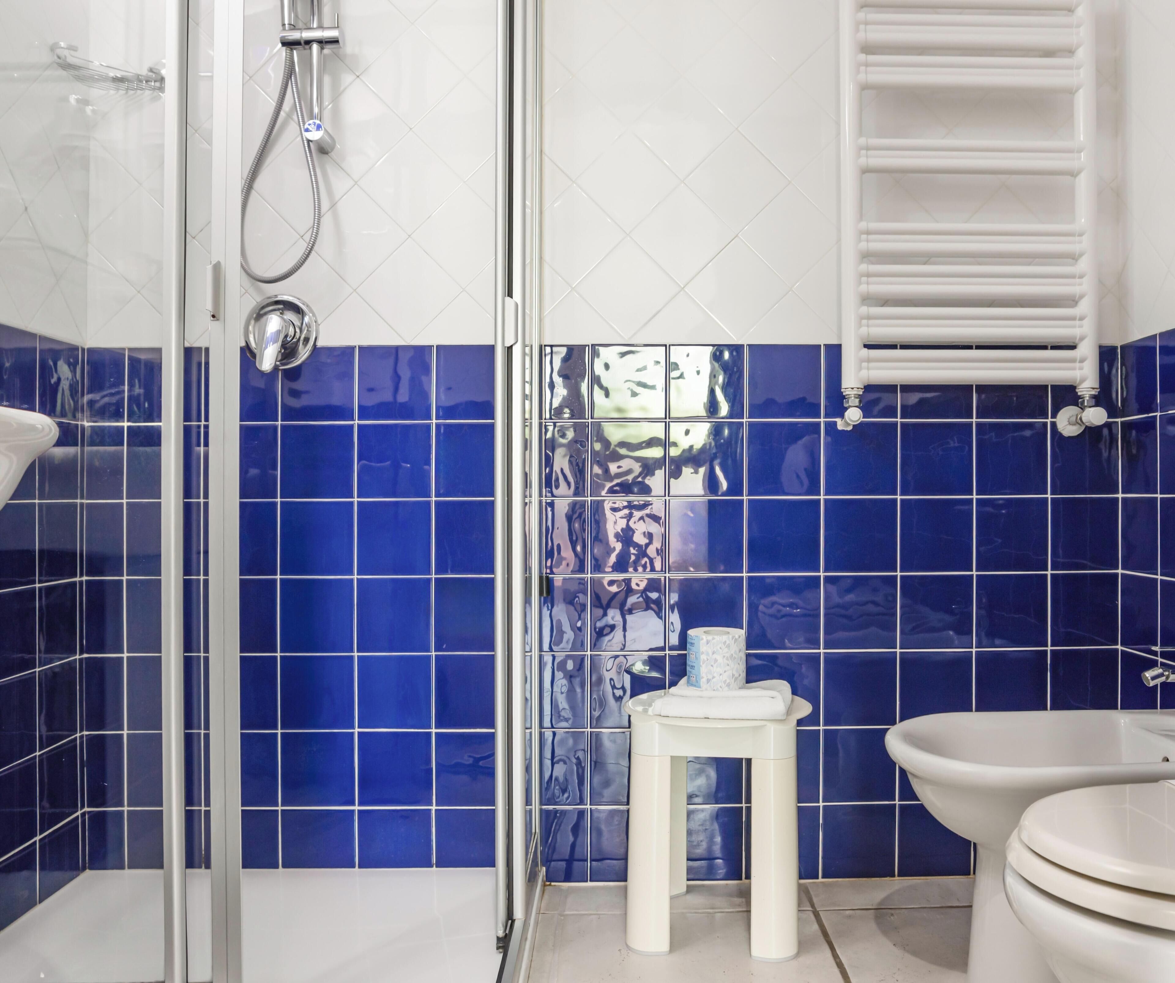 A bathroom with a glass shower enclosure, a white toilet, and blue-tiled walls.