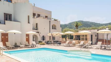 A pool area with lounge chairs and umbrellas, a bar, and a view of a mountain.