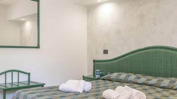 Una camera d'albergo con un letto, una testiera verde, un comodino, uno specchio e una poltrona verde.