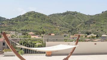 Eine Hängematte auf einem Balkon mit Blick auf eine hügelige Landschaft und Häuser.
