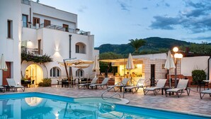 Ein Poolbereich mit Liegestühlen und Sonnenschirmen, eine Bar und ein Gebäude mit Balkon.
