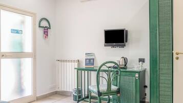 Una stanza piccola con una poltrona verde, un tavolo con un bollitore, una TV e una porta con maniglia.