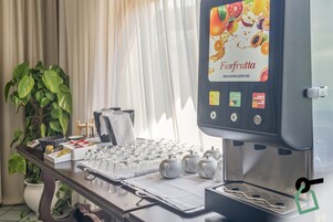 A juice dispenser with a fruit-themed label, a table with teapots and glasses, and a potted plant.