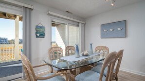 A dining area with a glass table surrounded by wicker chairs, a view of the outside, and a wall-mounted artwork of birds.