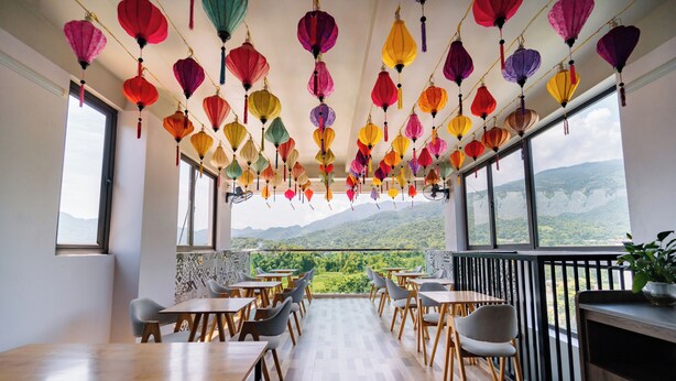 A restaurant with a terrace overlooking a mountainous landscape, featuring wooden tables and chairs, and colorful hanging lanterns. - Ha Giang City Hostel (Ha Giang 1)
