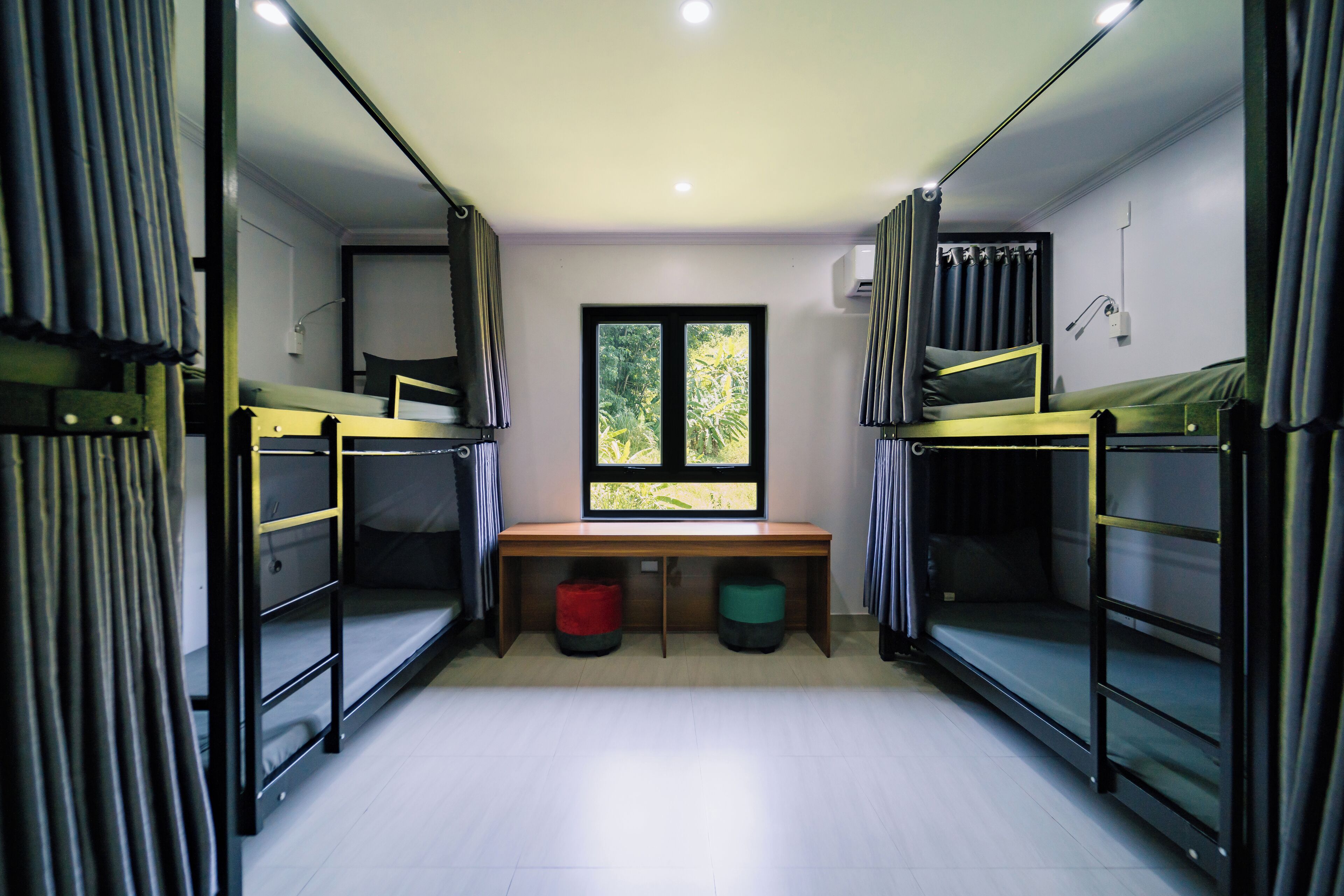 A dormitory room with bunk beds, a desk, and a window.