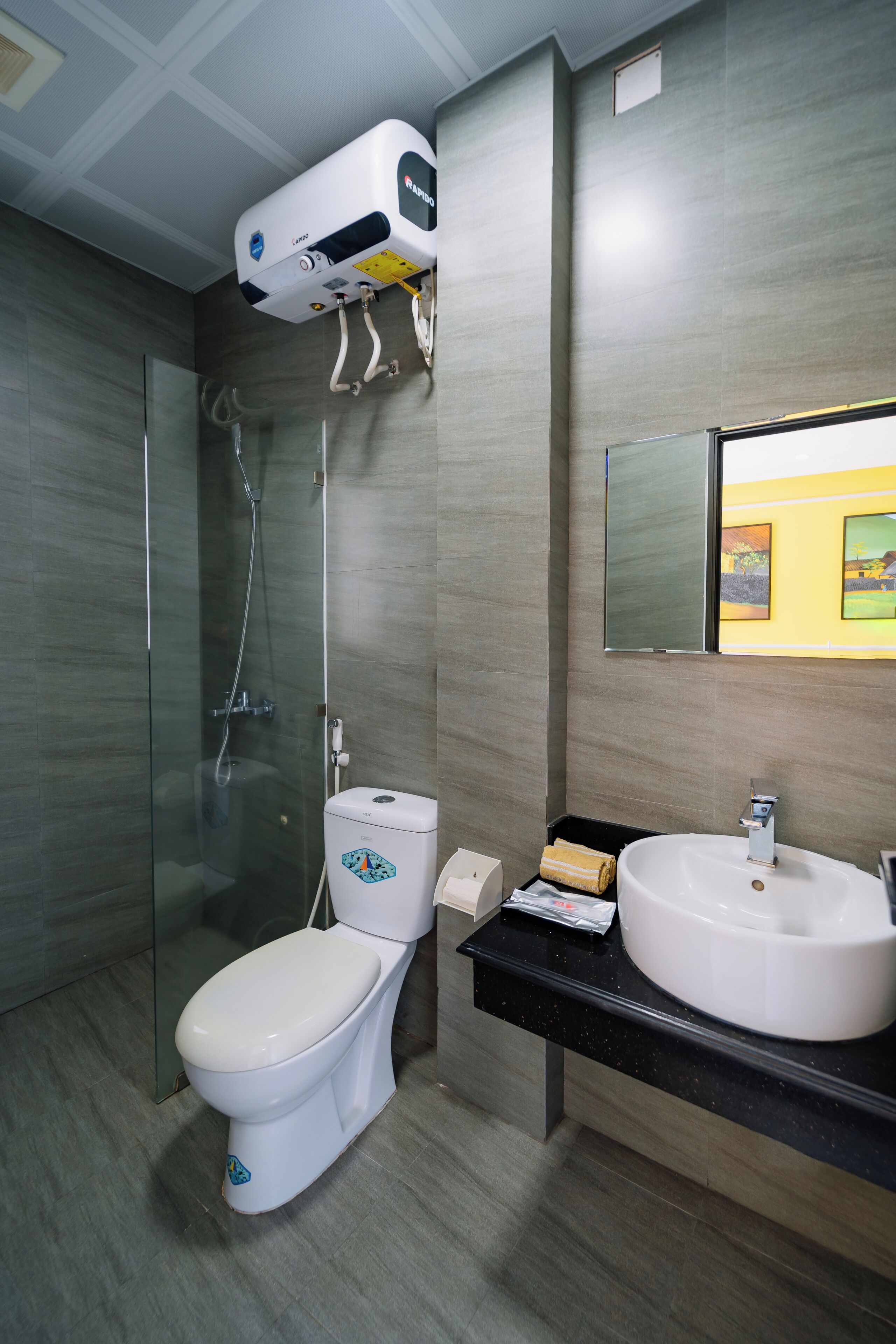 Un bagno moderno con doccia vetrata, un water bianco e un piano lavabo nero con lavello bianco.