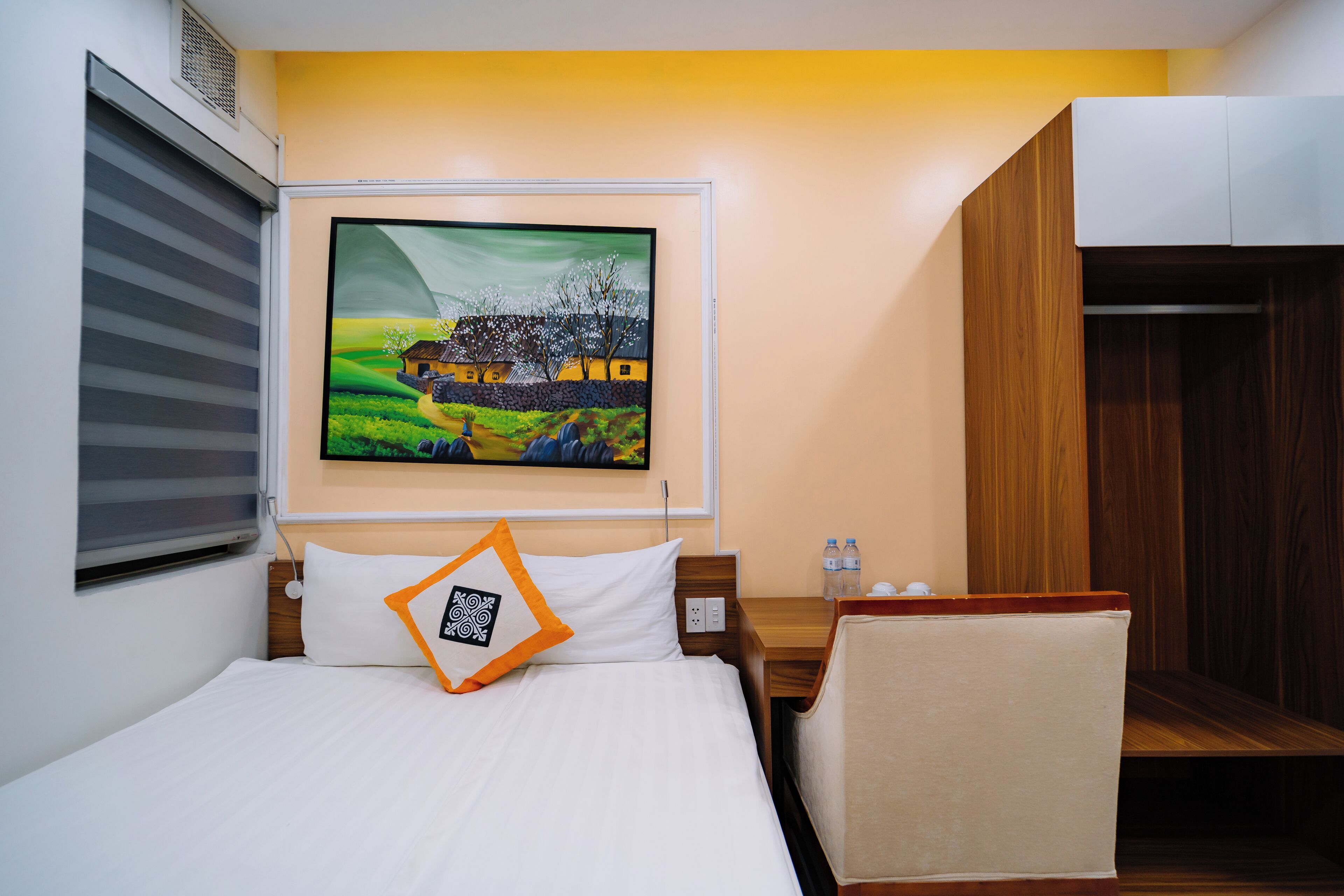 A hotel room with a bed, a nightstand, a chair, a painting on the wall, and a wardrobe.