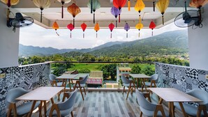 A balcony with tables and chairs, a sign for a fresh pizza pasta restaurant, and a view of green mountains. - Ha Giang City Hostel (Ha Giang 1)