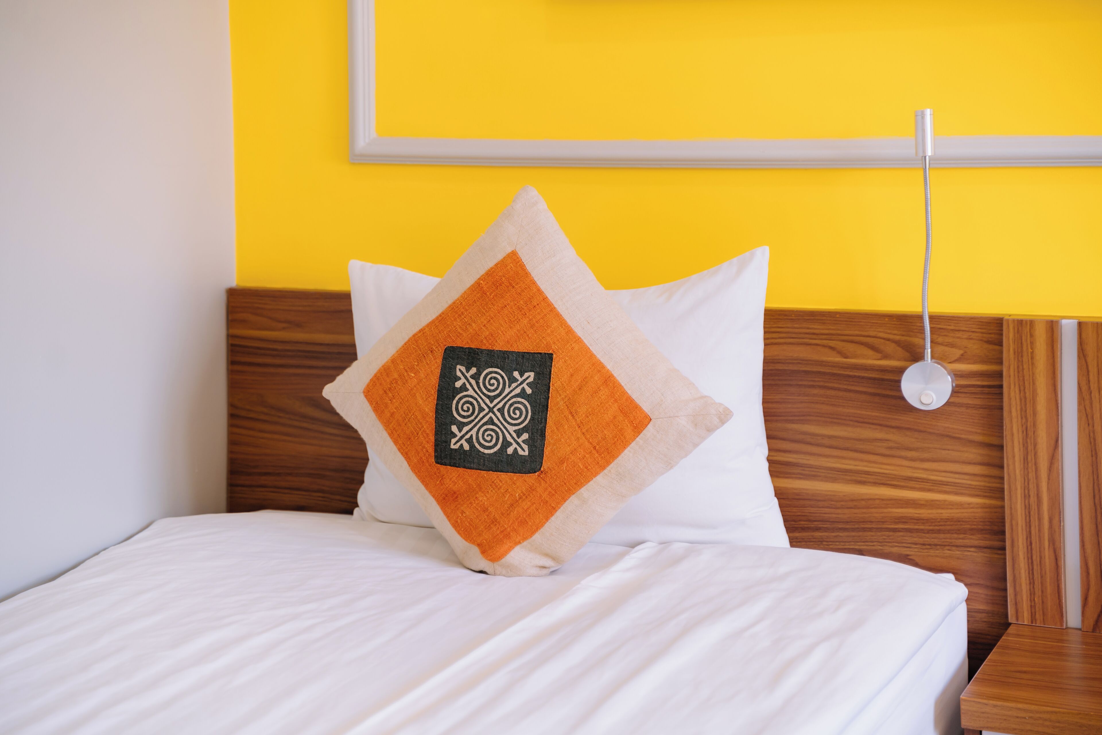 Una cama con ropa blanca, cabecera de madera y pared amarilla.