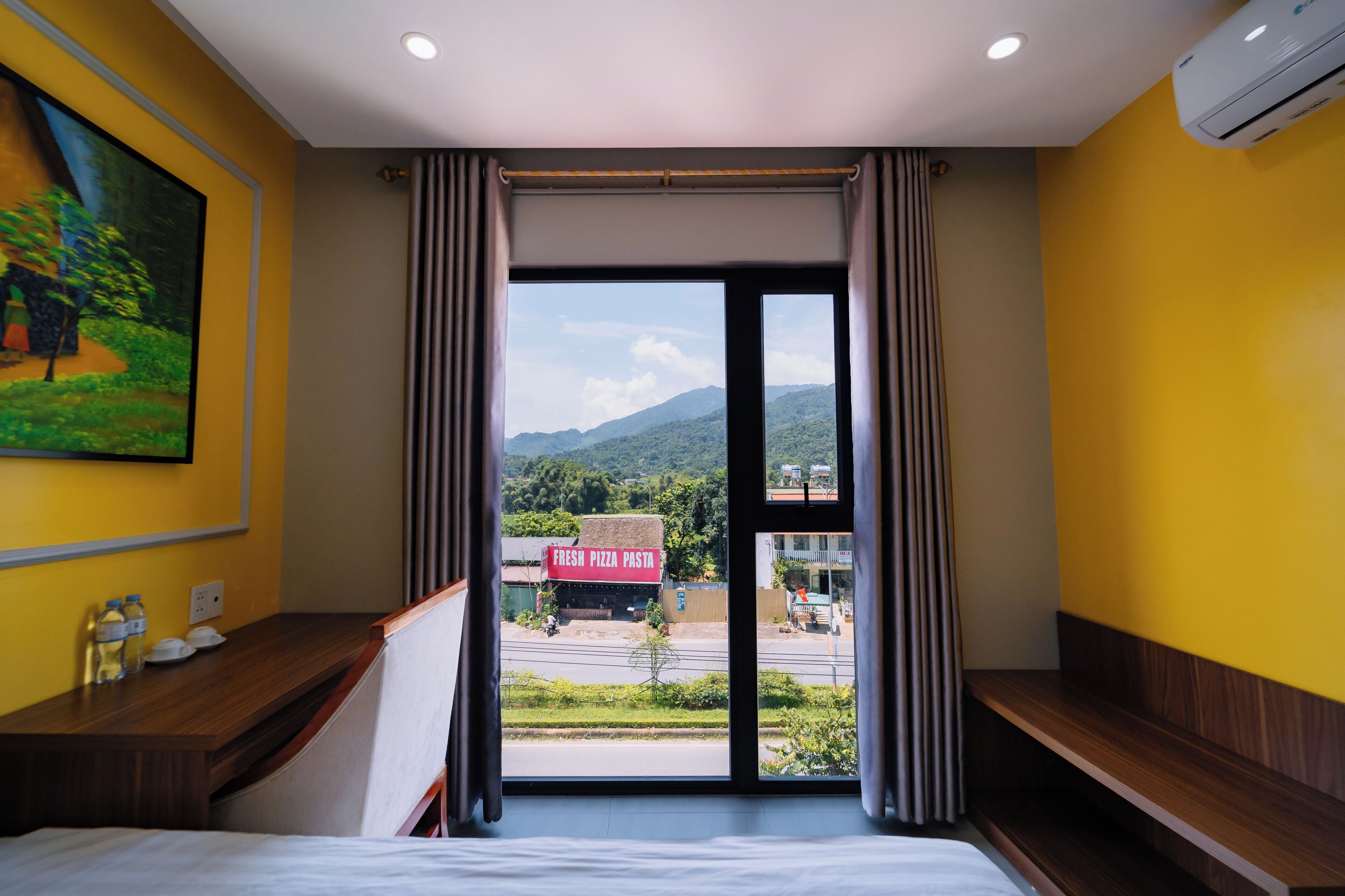 A hotel room with a bed, a desk, and a large window with curtains.
