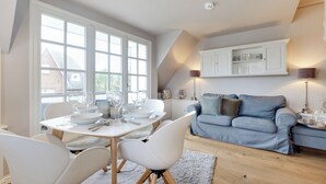 A modern kitchen with white cabinetry, a dining table set for six, and a blue sofa in the living area.