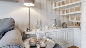 A modern living room with a grey sofa, a metallic tray with decorative items, a floor lamp, and a white shelving unit with storage.