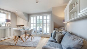 A modern kitchen with white cabinetry, a dining area with a white table and chairs, and a grey sofa in a living room.
