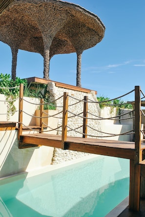 A pool area with a rope barrier, a wooden deck, and a stone wall. - Celestial Penthouse with Private Jacuzzi (Tulum)