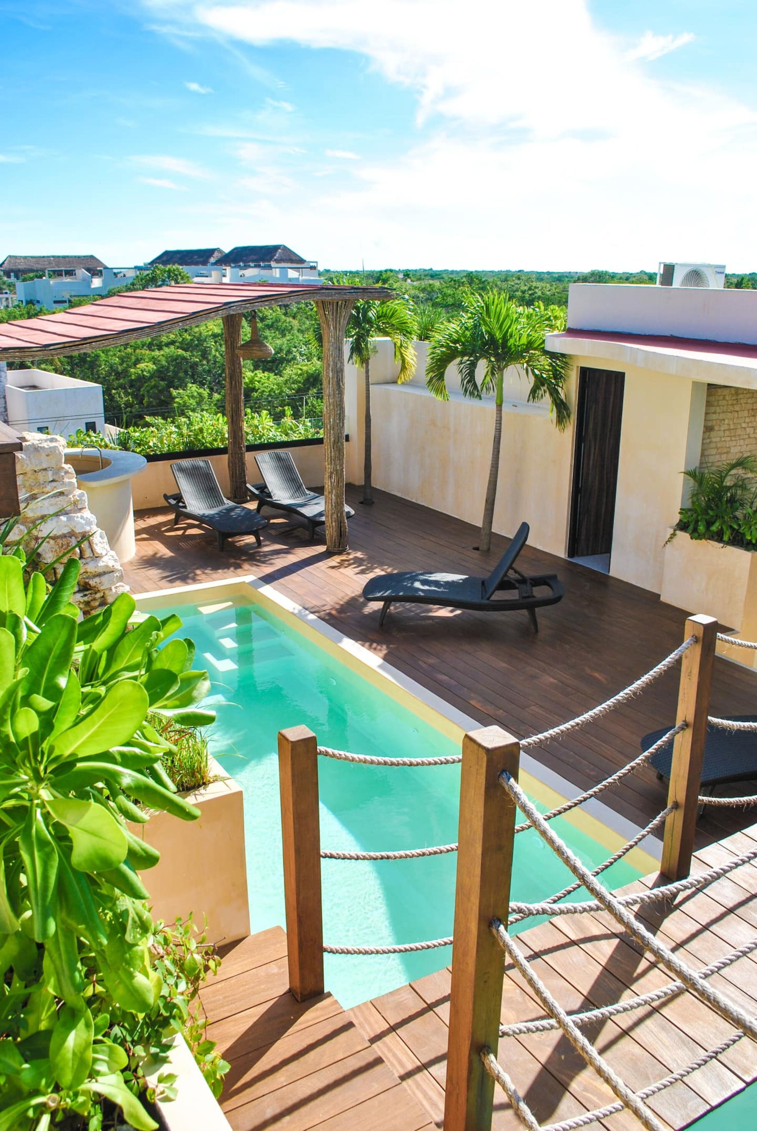 A rooftop pool area with lounge chairs, a wooden deck, and a view of the surrounding landscape.