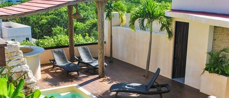 A rooftop pool area with lounge chairs, a wooden deck, and a view of the surrounding landscape.