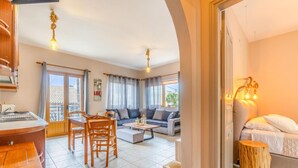 A spacious living area with a sofa, coffee table, and dining table. A kitchen area with a sink and counter is visible in the foreground. - Zante Apt in Gaios With 1 Bedrooms and 1 Bathrooms (Paxos)