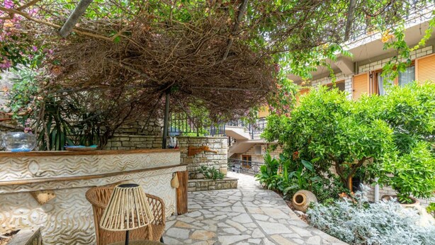 An outdoor patio area with stone flooring, a wicker table with a lamp, and lush greenery. - Zante Apt in Gaios With 1 Bedrooms and 1 Bathrooms (Paxos)