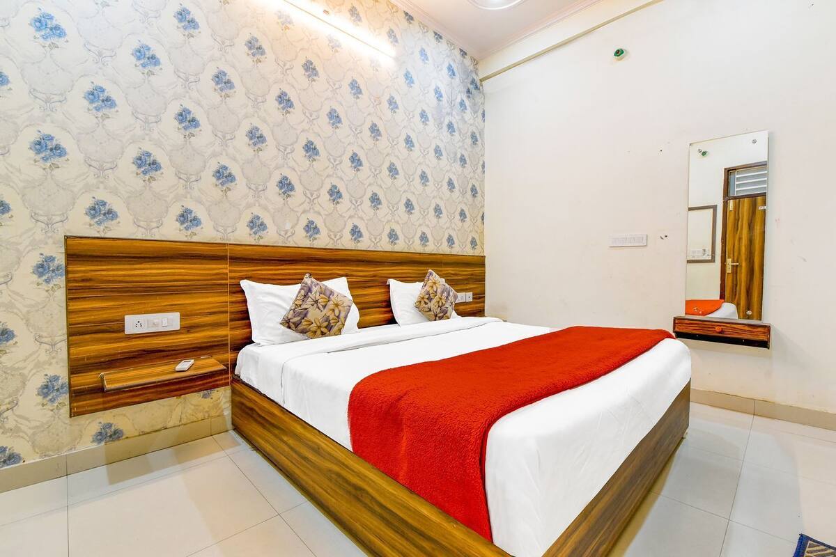 Une chambre d’hôtel avec une tête de lit en bois, un papier peint à motifs floraux, un plaid rouge et un miroir au mur.