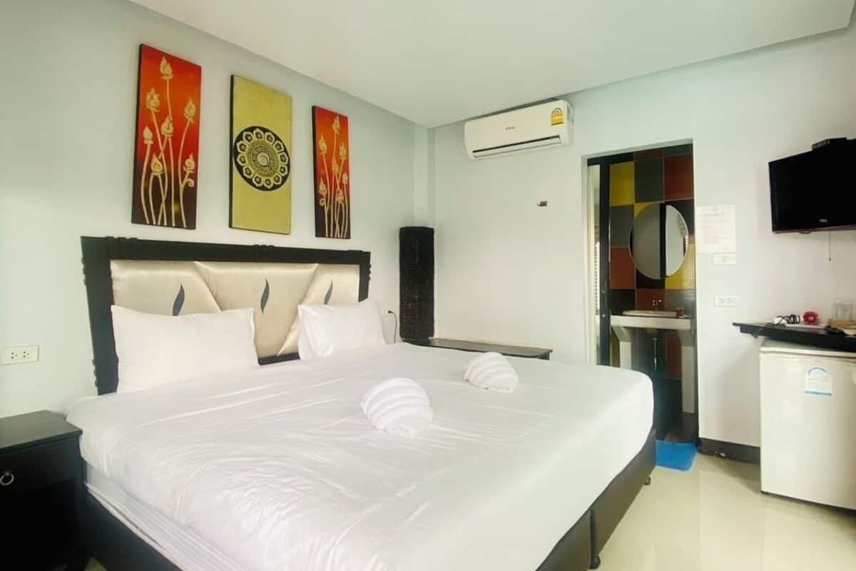 A hotel room with a large bed, a flat-screen TV, an air conditioning unit, and artwork on the walls.