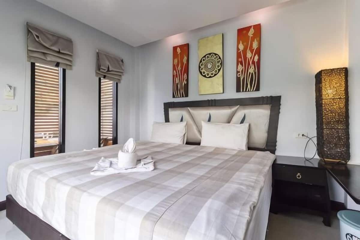 A neatly made bed with a checkered bedspread, a bedside table with a lamp, and artwork on the wall.