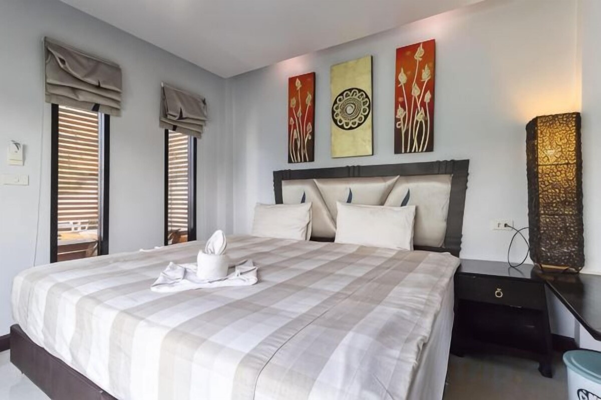 A neatly made bed with a checkered bedspread, a bedside table with a lamp, and artwork on the wall.