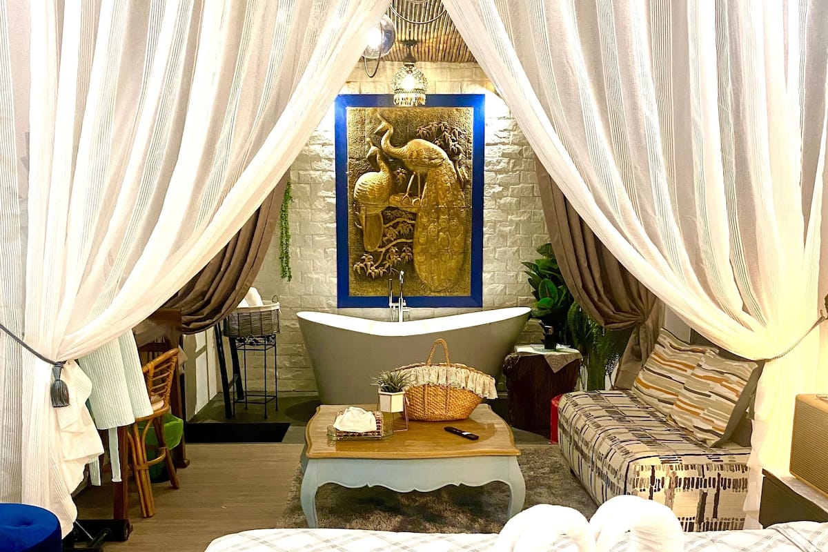 A bedroom with a bed, a bathtub, and a wall-mounted artwork.
