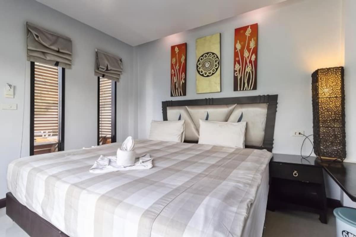 A neatly made bed with a checkered bedspread, a bedside table with a lamp, and artwork on the wall.