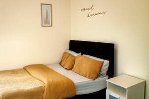 Un letto ben rifatto con una testiera nera e due cuscini, un comodino con un cassetto e un quadro appeso al muro.