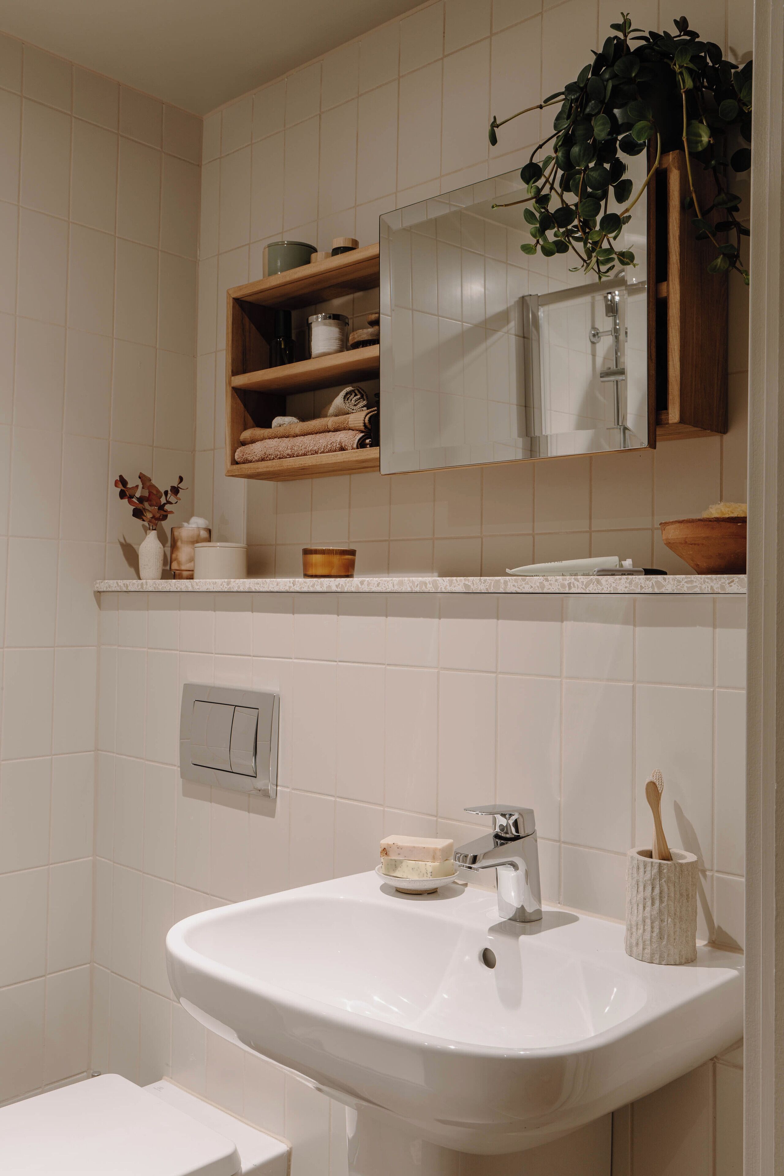 Une salle de bain avec un lavabo blanc, un miroir au-dessus et une étagère contenant des articles de toilette.