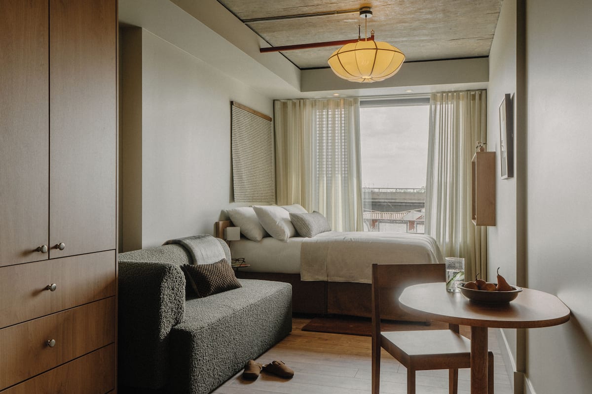 A compact hotel room with a bed, a sofa, a small table, and a wardrobe.