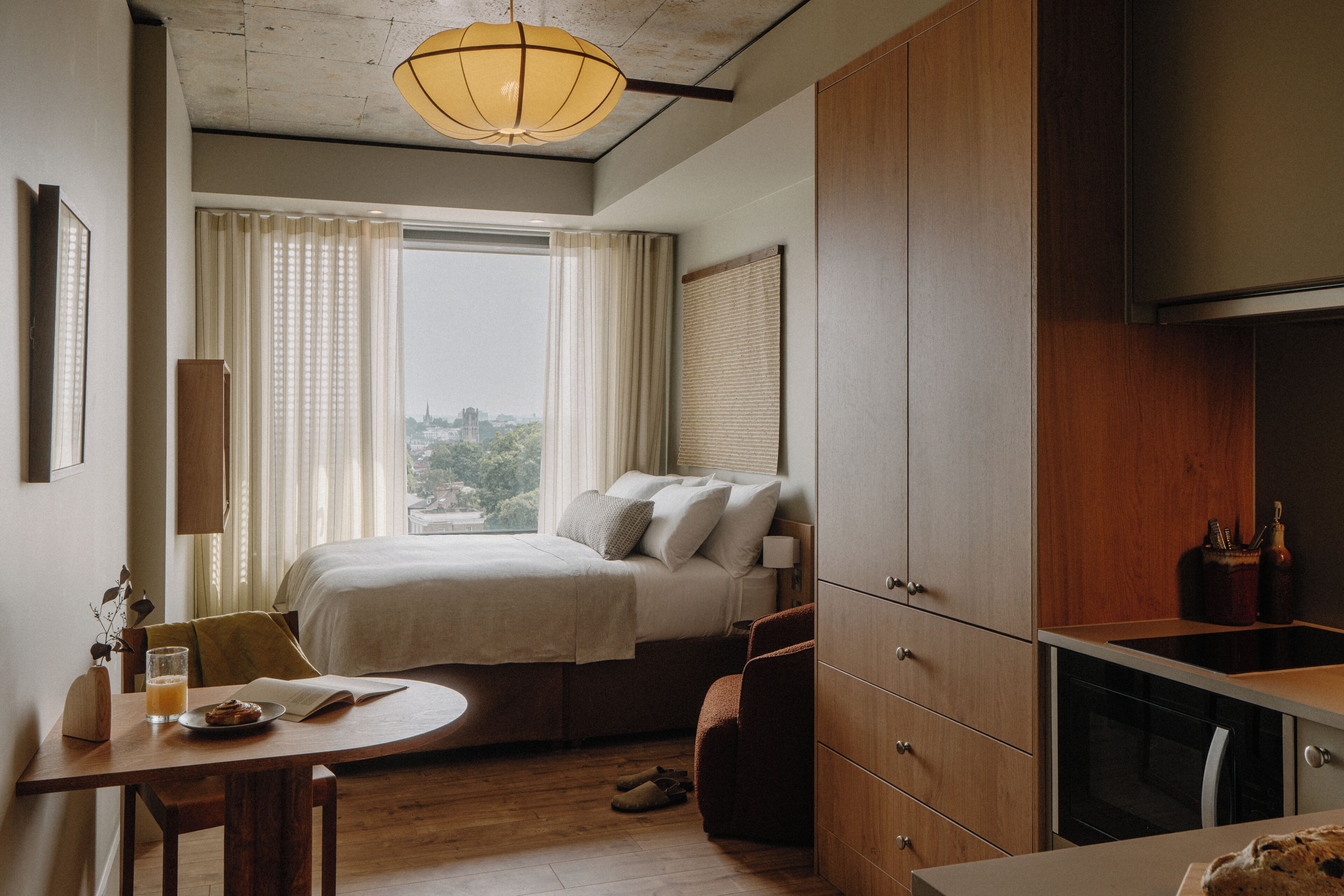 A bedroom with a bed, bedside table, and a view of the city.
