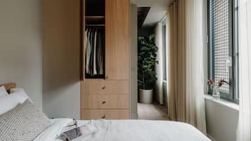 A bedroom with a bed, a wooden wardrobe, a potted plant, and a window with curtains.