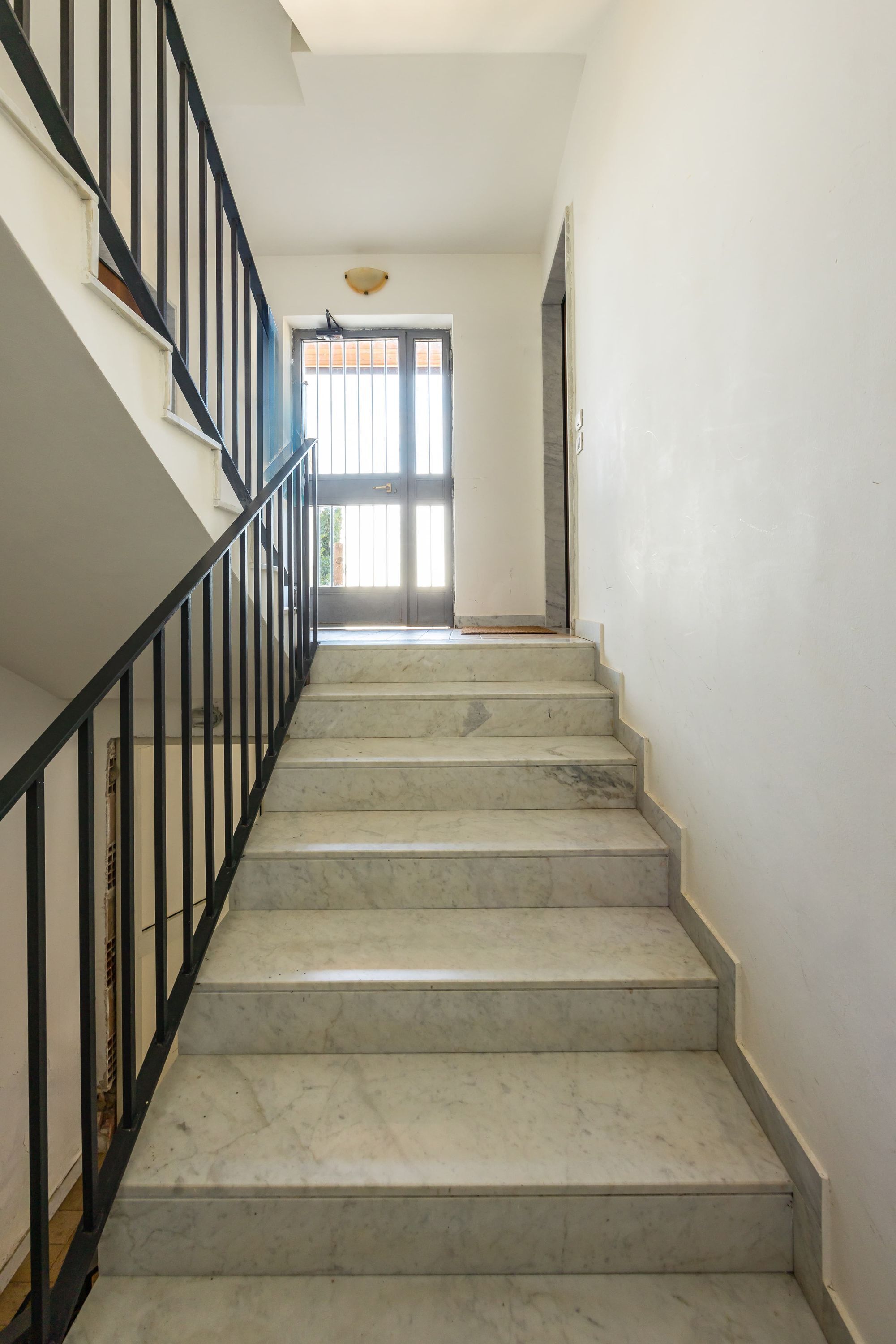 A staircase with marble steps and black railings leading to a door with a window.