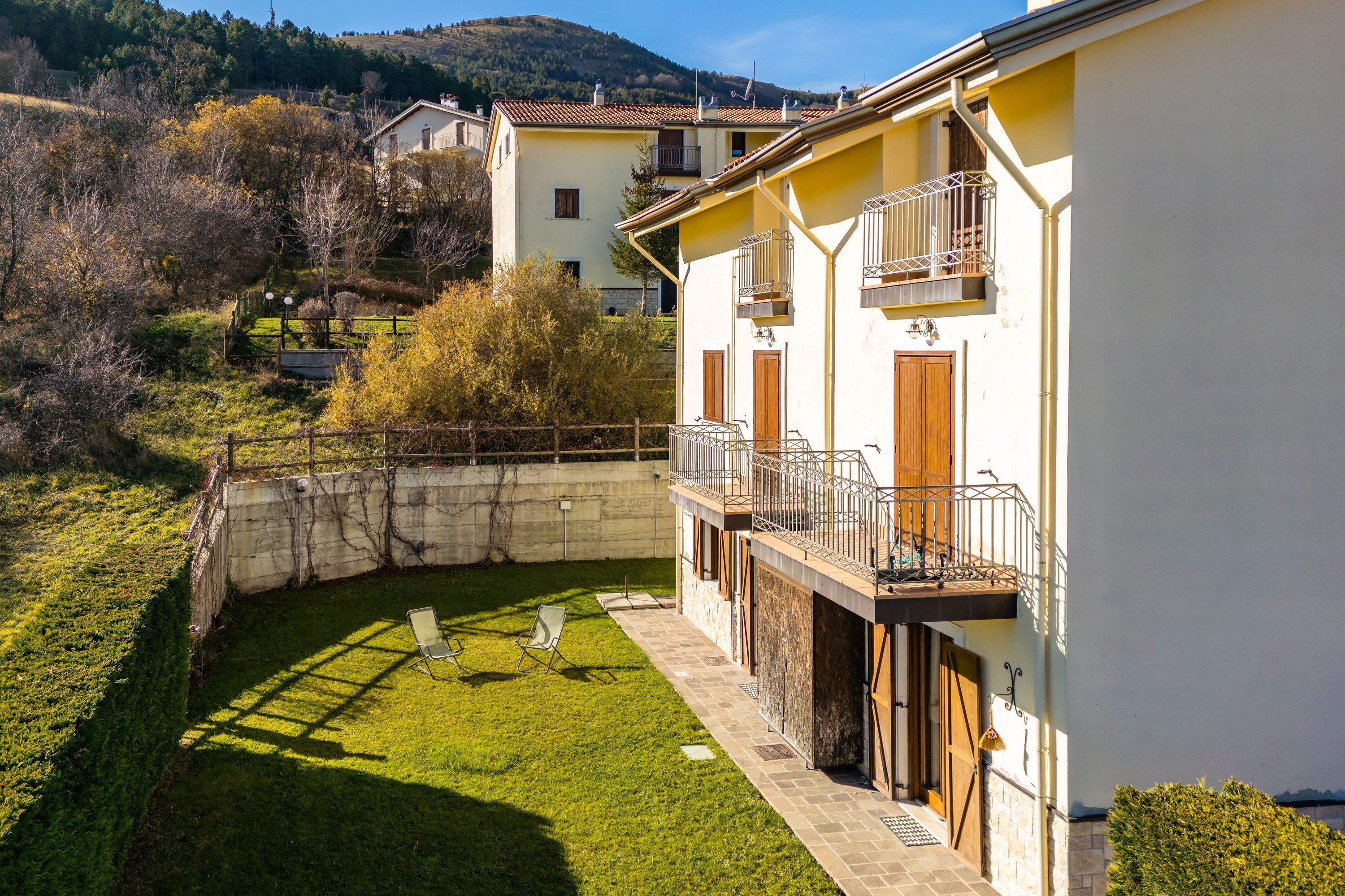Ein zweistöckiges Gebäude mit Balkon, einem kleinen Garten und Blick auf die umliegende Landschaft.