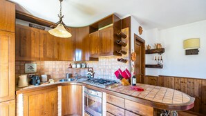 A kitchen with wooden cabinets, a gas stove, a sink, and a hanging light fixture. - Rifugio Marley in Pescocostanzo (Pescocostanzo)