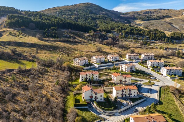 An aerial view of a residential area with multiple apartment buildings, roads, and green hills in the background. - Rifugio Marley in Pescocostanzo (Pescocostanzo)